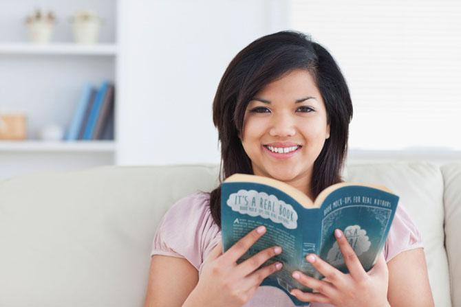 free book mock up - woman holding paperback book on couch