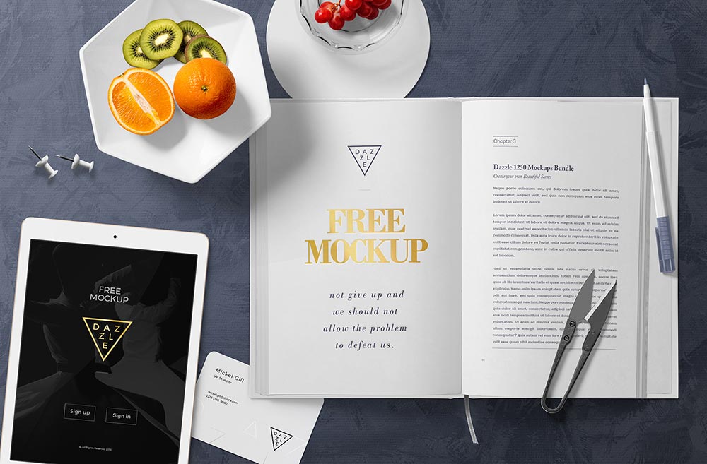 A modern workspace with a digital tablet displaying a graphic, a hardcover book page mockup of a motivational chapter, alongside a collection of fresh fruits and decorative items on a sleek dark surface.