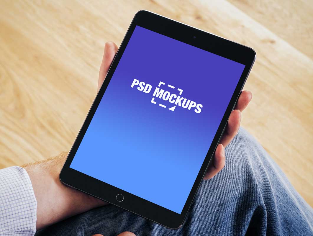 A person sitting down, holding a tablet mockup displaying a screen with the words "psd mockups" on a blue background.
