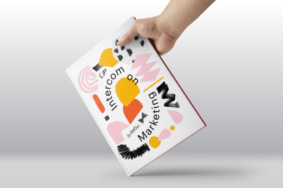 Hand holding a book with an abstract art cover design, featuring the words "intercom on marketing".