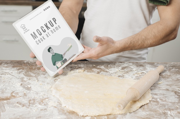 Man Holding Book and Rolling Dough in the Kitchen