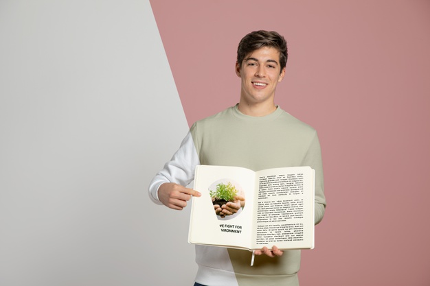 A smiling young man holding an open book with content visible on the right page, against a split background of white and pink.