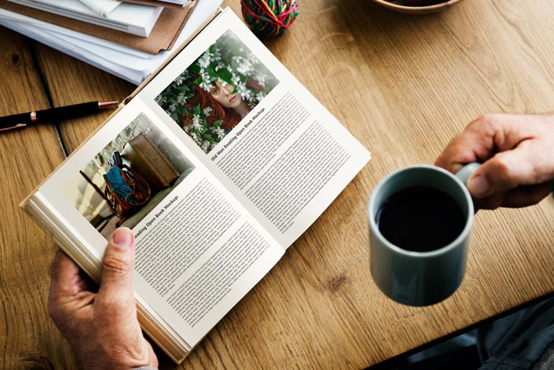 A man enjoying a fresh cup of coffee while reading an open book featuring articles and vibrant photography.