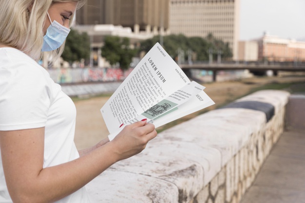 Frau mit Maske liest ein Buch auf der Straße