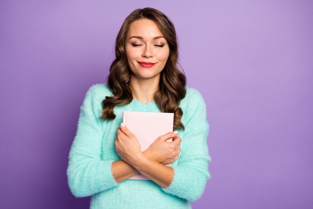 Woman smiling contentedly while holding a book to her chest against a purple background.